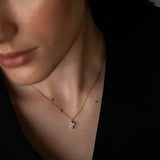 Close-up of a woman wearing a gold necklace with a small diamond pendant and matching earrings, dressed in black.