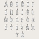 Collection of silver alphabet pendants, each adorned with sparkling gemstones, displayed on a light beige background.